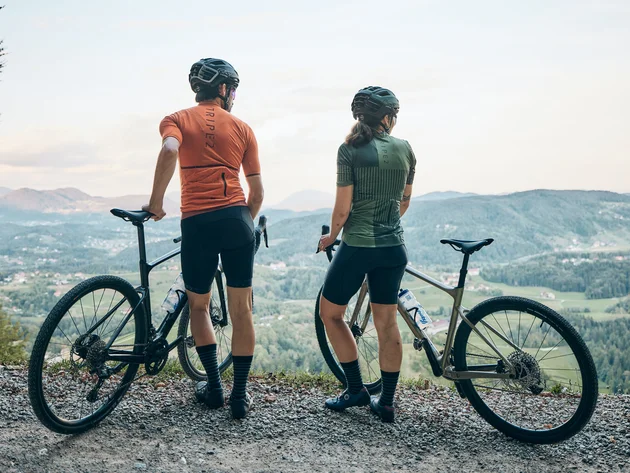 Qualitätsversprechen © Tobias Köhler Zwei Radfahrer halten ihre Fahrräder und blicken auf eine Berglandschaft
