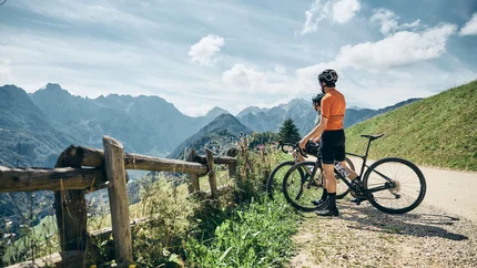 Zwei Radfahrer stehen an einem Bergweg und blicken auf die Berglandschaft
