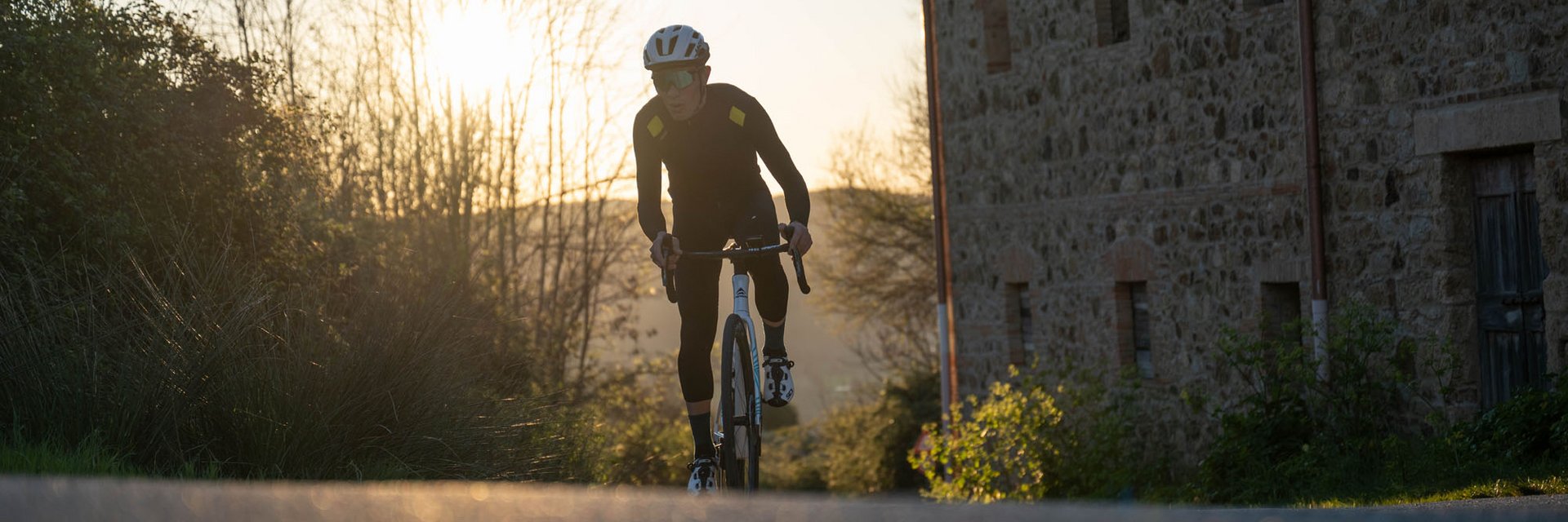 Radfahrer in schwarzer Kleidung fährt auf Landstraße bei Sonnenuntergang