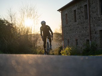 Cyclist in black riding on country road during sunset