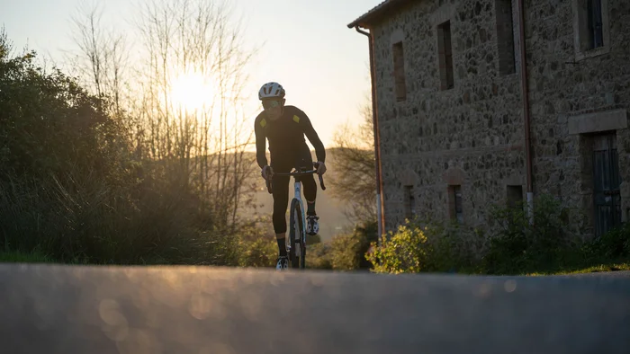 Gravelbiken in der Toskana © Tenuta il Cicalino Radfahrer in schwarzer Kleidung fährt auf Landstraße bei Sonnenuntergang