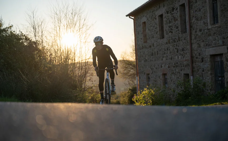 Gravelbike Urlaub in der Toskana © Tenuta il Cicalino Radfahrer in schwarzer Kleidung fährt auf Landstraße bei Sonnenuntergang