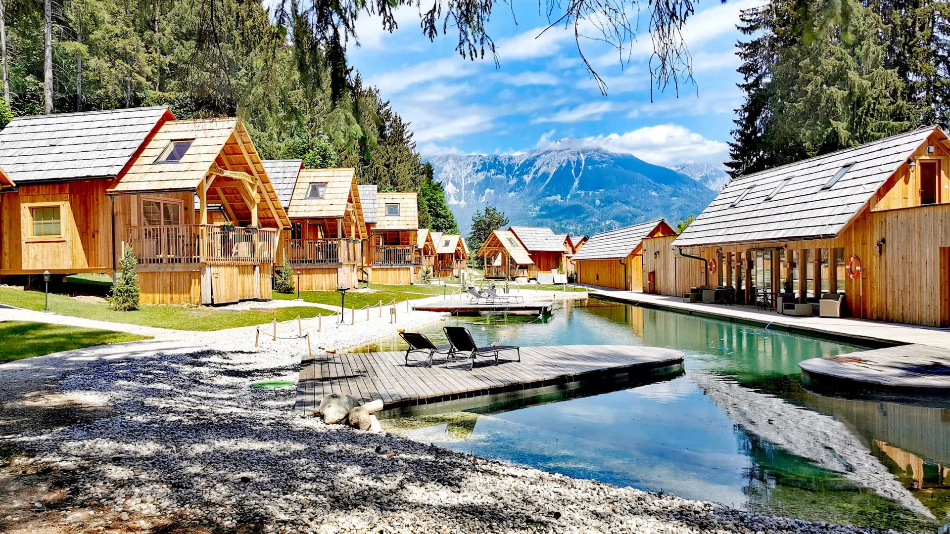 Wooden cabins by a lake with mountain view and lounge chairs on dock