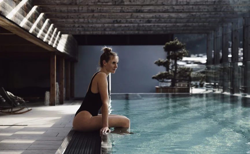 Dips&Drops - HOTEL · SPORTS · SPA · RESTAURANTS ****S © Matthias Warter Woman in black swimsuit sitting at the edge of a pool in a modern room