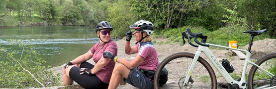 Two female cyclists resting on a log by the riverbank