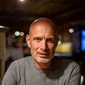 Older man in gray t-shirt sitting at table in warmly lit room
