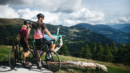 Zwei Radfahrer schauen auf eine Infotafel in den Bergen an einem sonnigen Tag