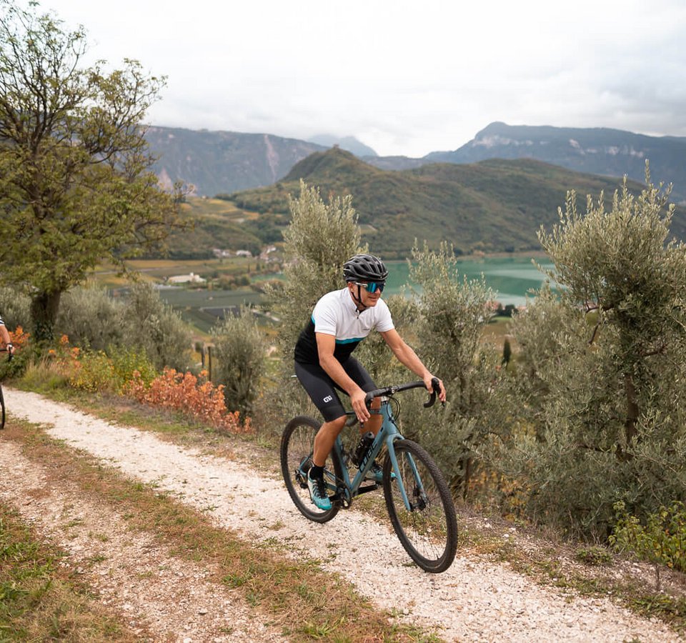 Genuss & Gravel in Tramin © Patrick Schwienbacher Zwei Radfahrer auf einem Weg in bergiger Landschaft mit See im Hintergrund