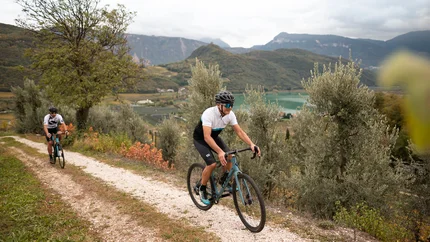Two cyclists riding on a path in mountainous landscape with lake background