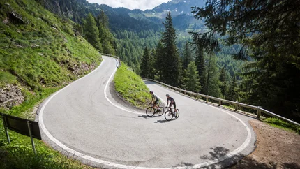 Two cyclists on a hairpin road in a mountainous forest area