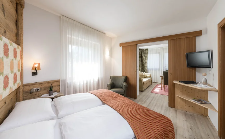 Gemütliches Hotelzimmer mit Doppelbett, Sessel und angrenzendem Wohnzimmer
