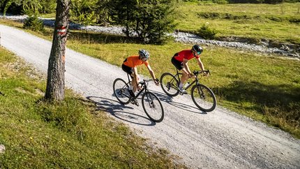 Two cyclists riding on a forest trail in the mountains under clear sky