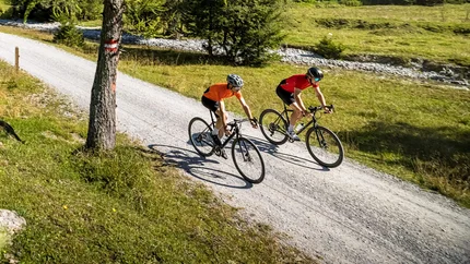 Zwei Radfahrer fahren auf einem Waldweg in den Bergen bei klarem Himmel