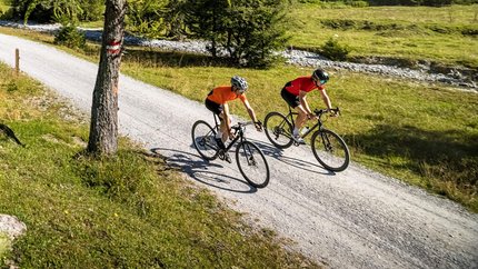 Zwei Radfahrer fahren auf einem Waldweg in den Bergen bei klarem Himmel