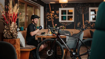 Radfahrer in schwarzer Ausrüstung trinkt Kaffee neben seinem Fahrrad in Café