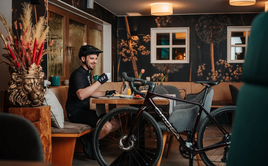 Radfahrer in schwarzer Ausrüstung trinkt Kaffee neben seinem Fahrrad in Café