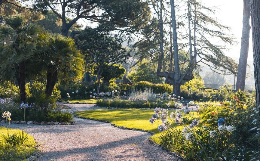 Weg durch blühenden Garten mit Bäumen und Sonnenlicht