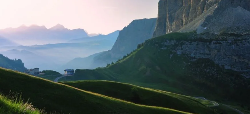 Blick auf grüne Hügel und steile Felsen in den Bergen bei Sonnenaufgang