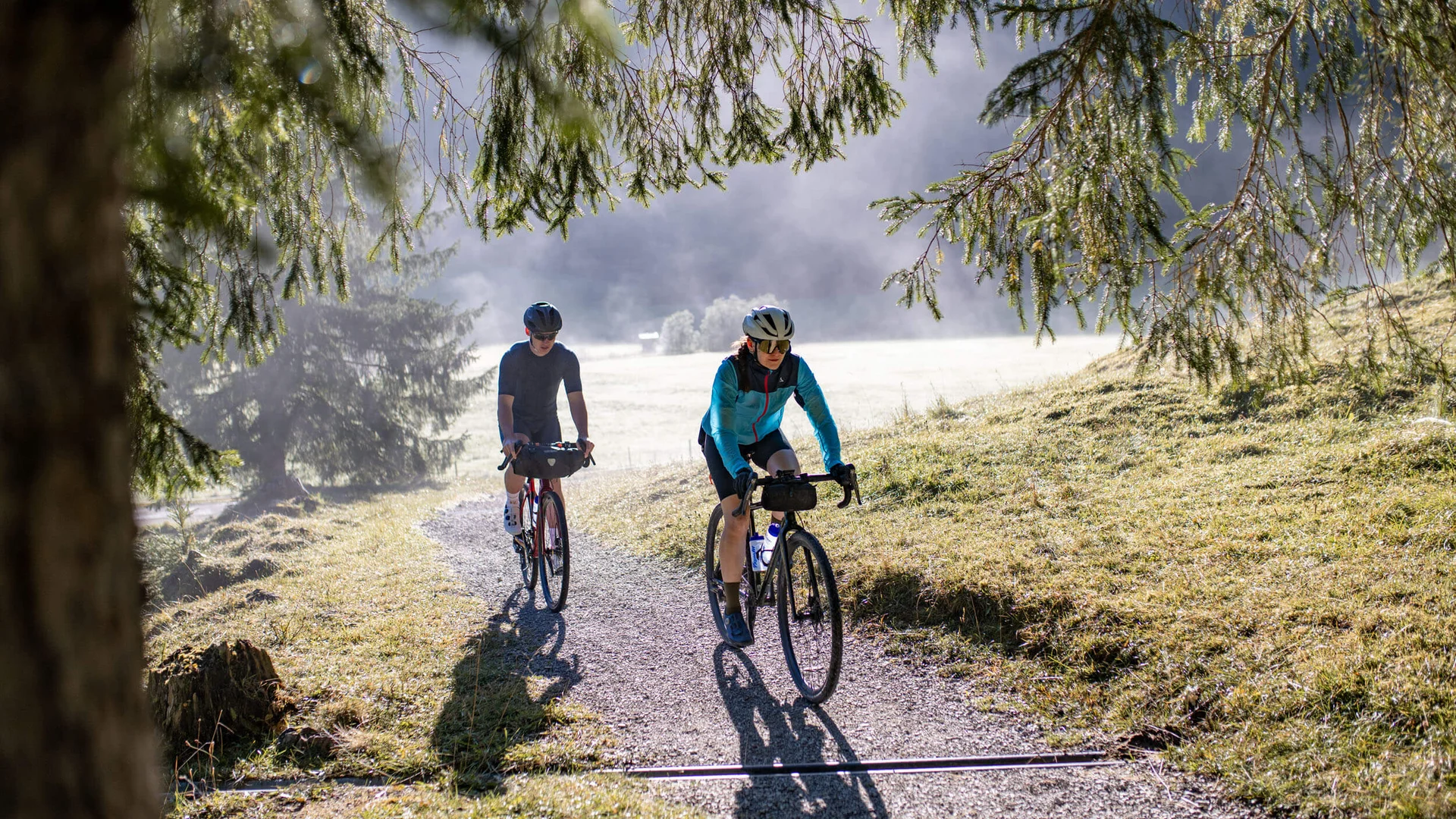 Zwei Radfahrer fahren auf einem schmalen Waldweg im Morgenlicht