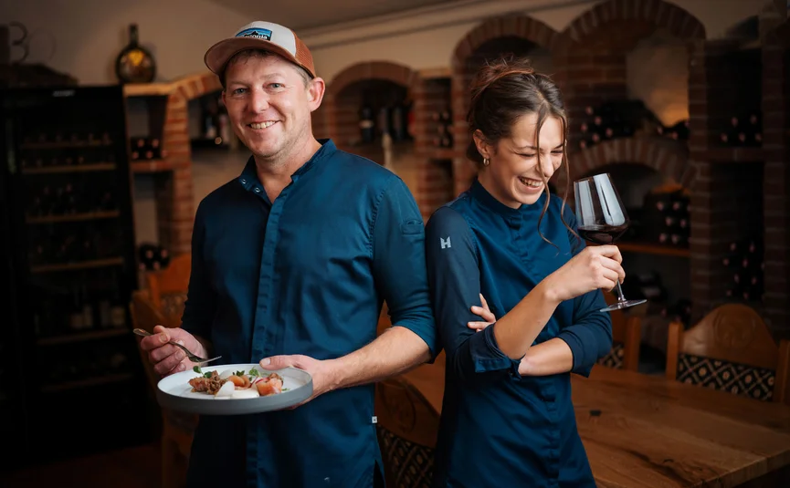 Bike Boutique Hotel Lindenhof **** © Martin Hofmann Zwei lächelnde Menschen in blauen Hemden mit Essen und Wein in einem Weinkeller