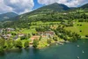 Lake shore with beach, sun loungers, and tennis courts by forested mountains