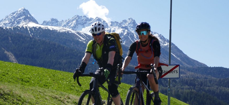 Zwei Radfahrer fahren auf Landstraße mit Bergen im Hintergrund