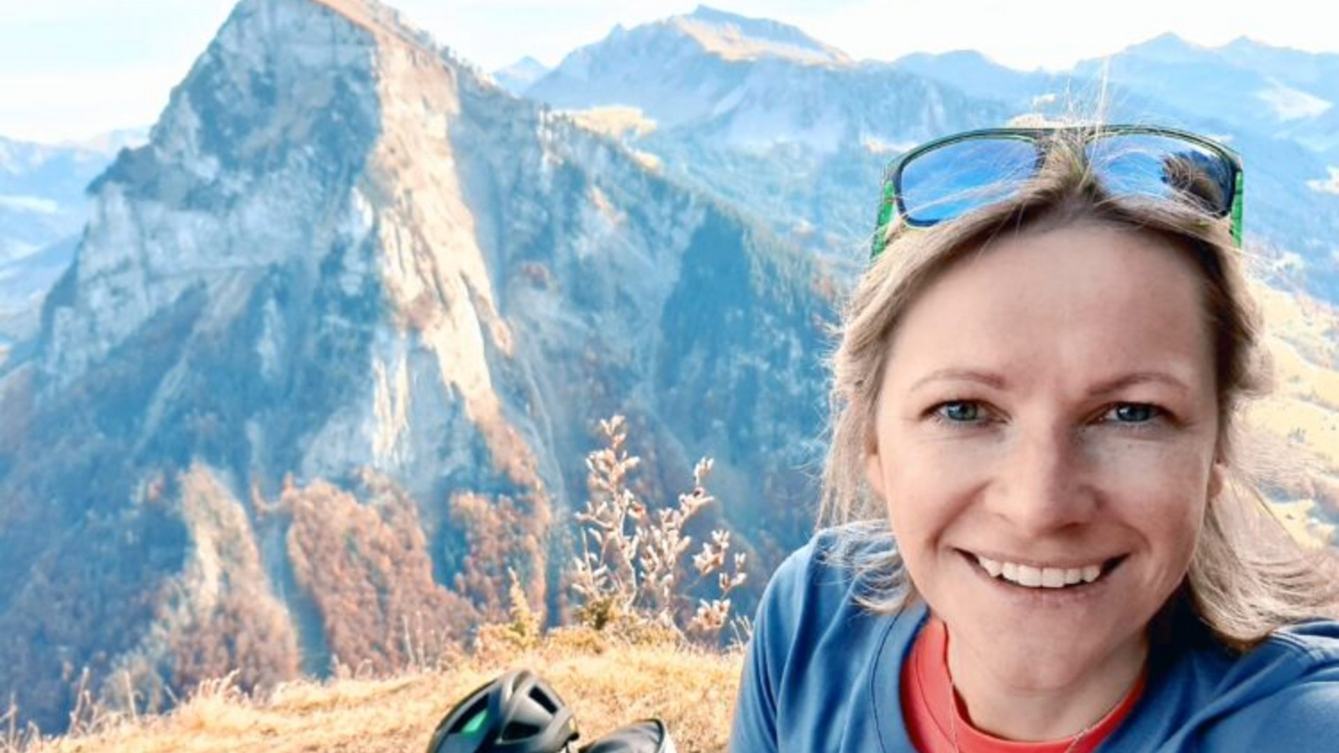 Frau macht Selfie auf Berggipfel mit Helm und Sonnenbrille