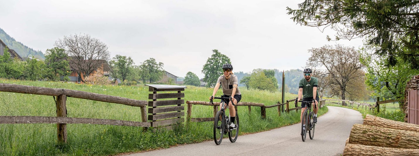 Graveltour Brandnertal © Chris Gollhofer - Vorarlberg Tourismus Zwei Radfahrer auf Landstraße mit grünen Wiesen und Bäumen im Hintergrund