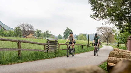 Two cyclists on a country road with green fields and trees in the background