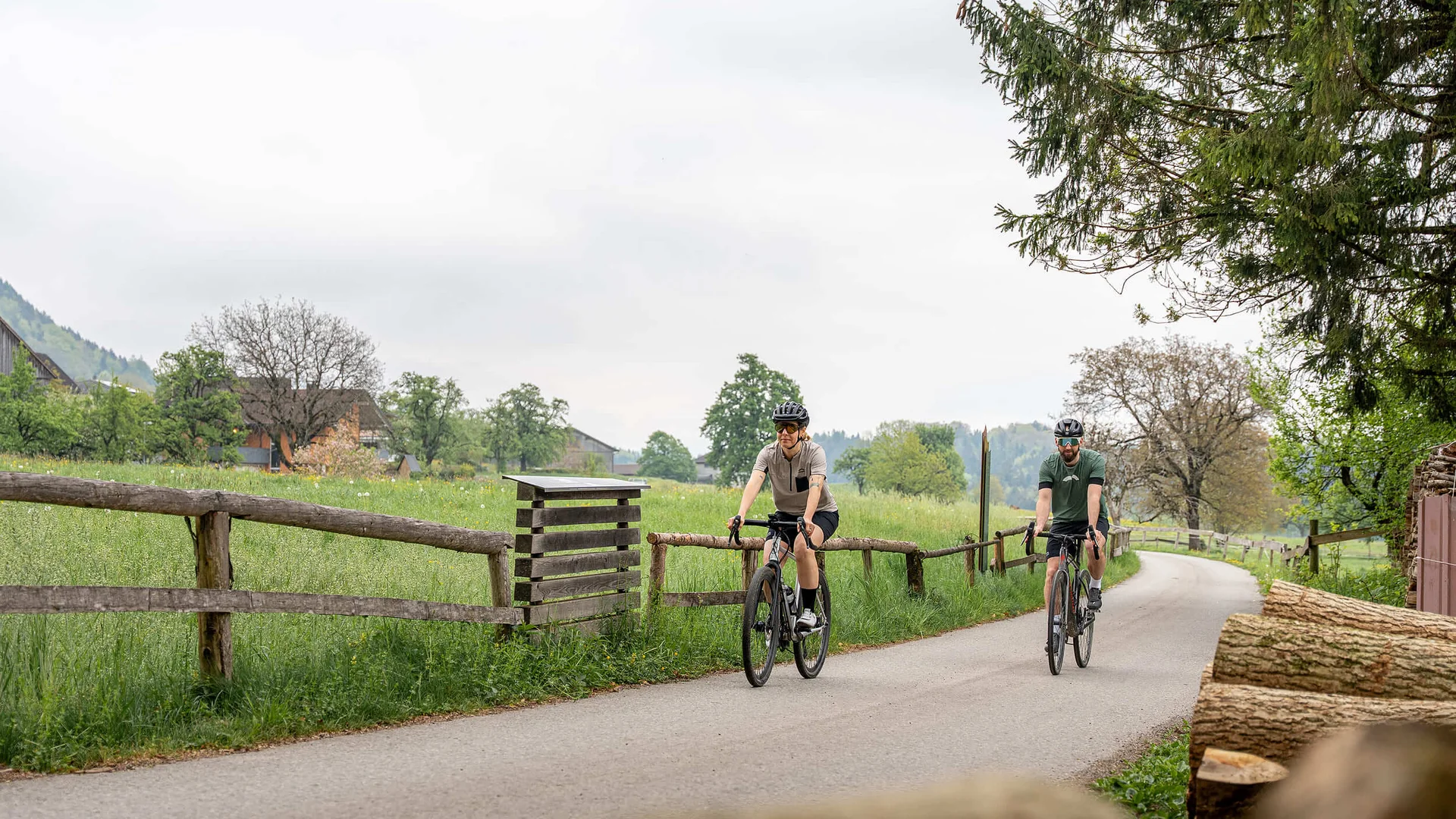 Gravelbiken in Vorarlberg: Die 7 schönsten Highlights zwischen Bodensee und Alpen © Chris Gollhofer - Vorarlberg Tourismus Zwei Radfahrer auf Landstraße mit grünen Wiesen und Bäumen im Hintergrund