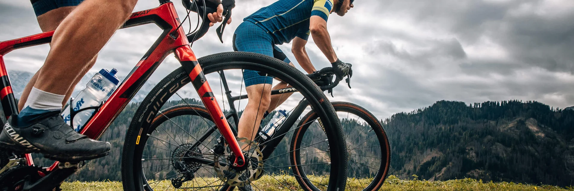 Two cyclists riding on a mountain trail under cloudy sky