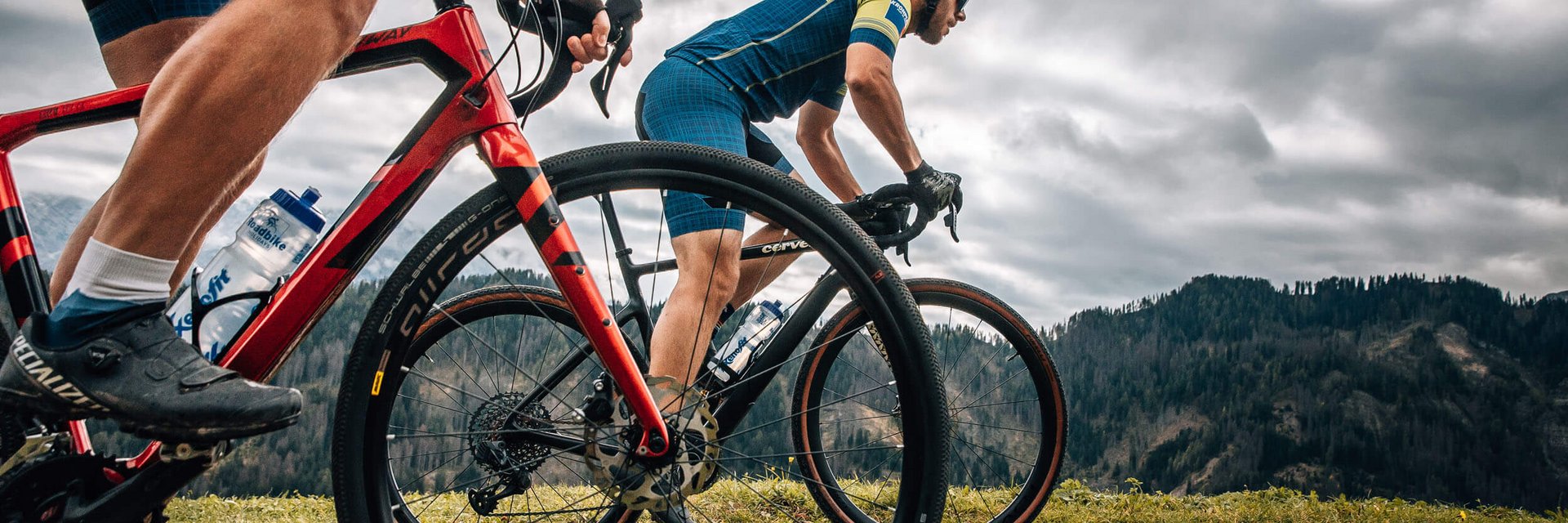 Two cyclists riding on a mountain trail under cloudy sky
