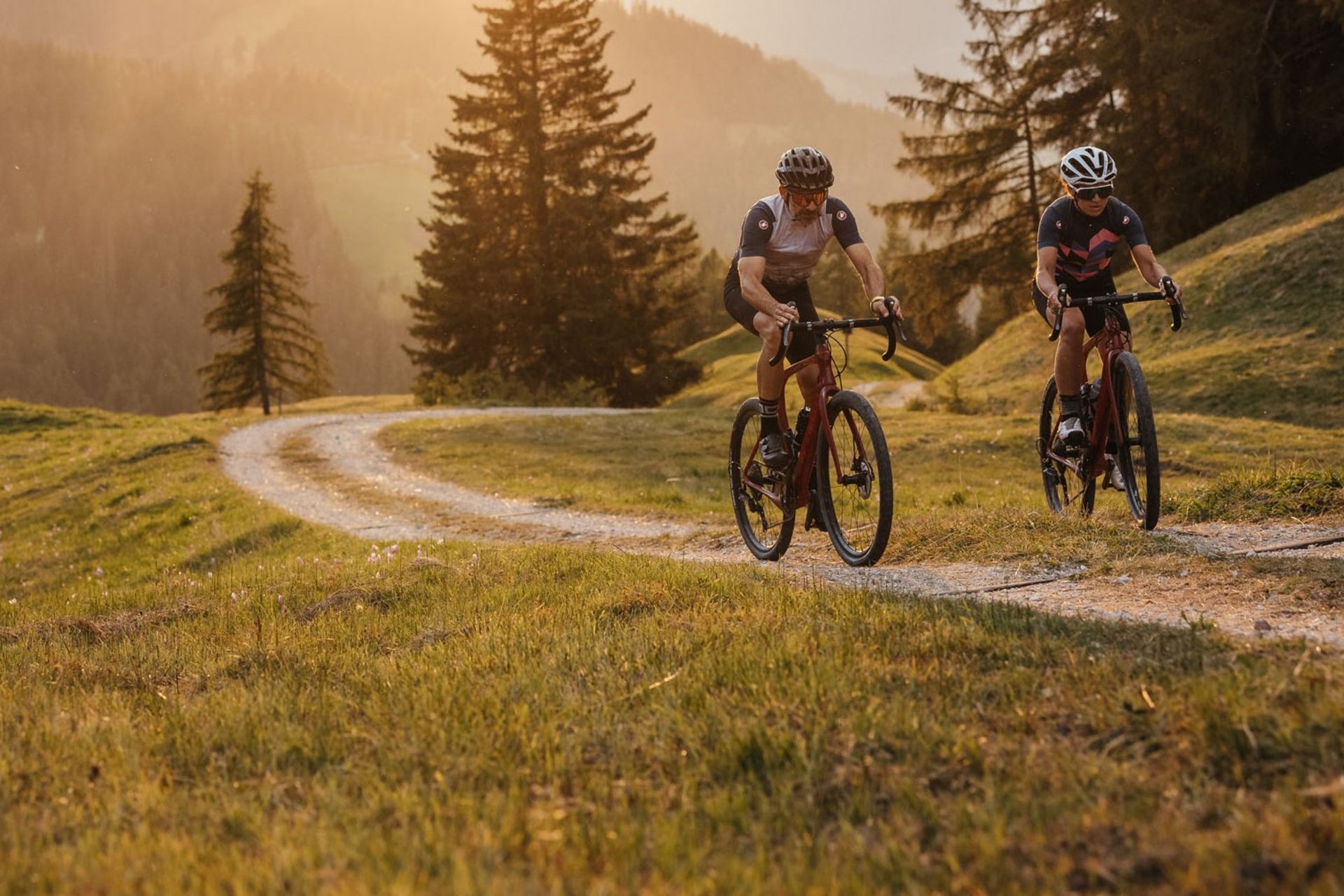 Zwei Radfahrer fahren auf einem Waldweg bei Sonnenuntergang in den Bergen