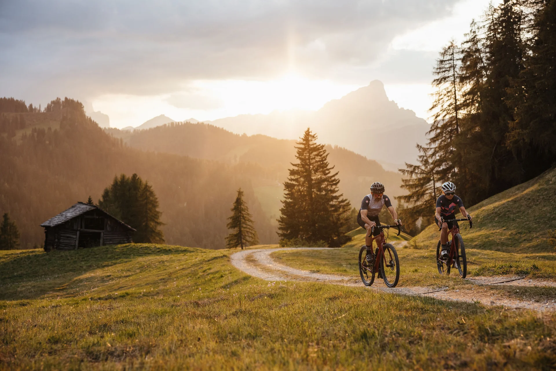 Gravelbike Holidays © Alex Moling Zwei Radfahrer fahren auf einem Waldweg bei Sonnenuntergang in den Bergen