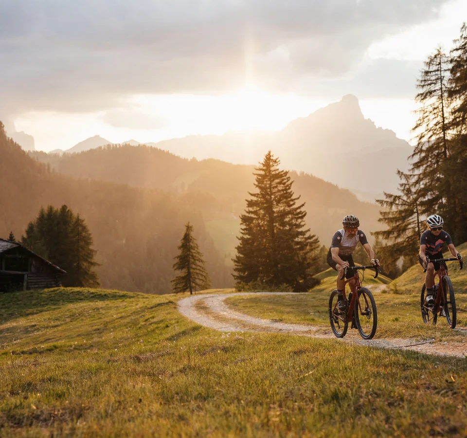 5 Gravelbike-Touren in Alta Badia, die du gefahren haben solltest © Alex Moling Zwei Radfahrer fahren auf einem Waldweg bei Sonnenuntergang in den Bergen
