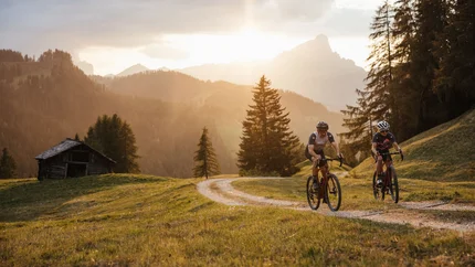 Two cyclists riding on a forest trail at sunset in the mountains