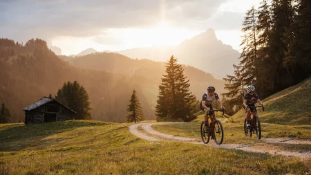 Two cyclists riding on a forest trail at sunset in the mountains