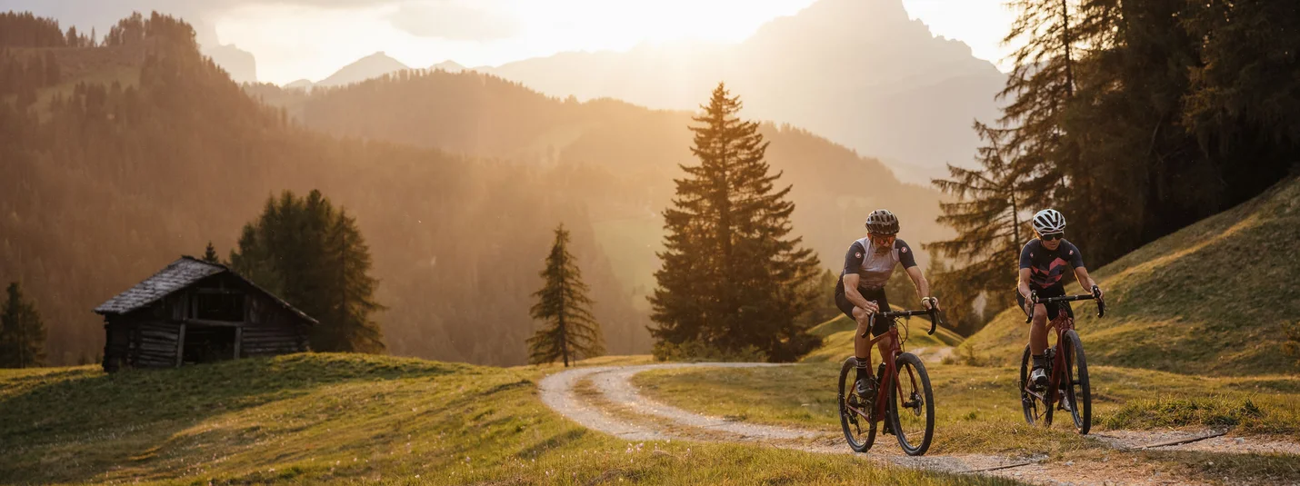 Gravel bike holidays in South Tyrol © Alex Moling Two cyclists riding on a forest trail at sunset in the mountains