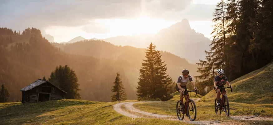 Zwei Radfahrer fahren auf einem Waldweg bei Sonnenuntergang in den Bergen