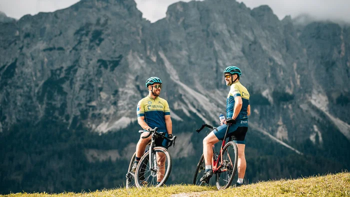 Two cyclists talking on their bikes in front of mountain scenery