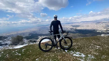 Bikepacking von Wien nach Athen © Jan Koller Radfahrer mit Helm auf schneebedecktem Berg mit Stadtpanorama im Hintergrund