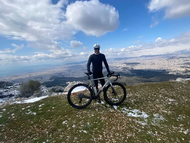 Bikepacking von Wien nach Athen © Jan Koller Radfahrer mit Helm auf schneebedecktem Berg mit Stadtpanorama im Hintergrund