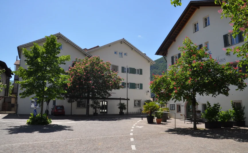 Straßenecke mit weißen Häusern und blühenden Bäumen unter blauem Himmel