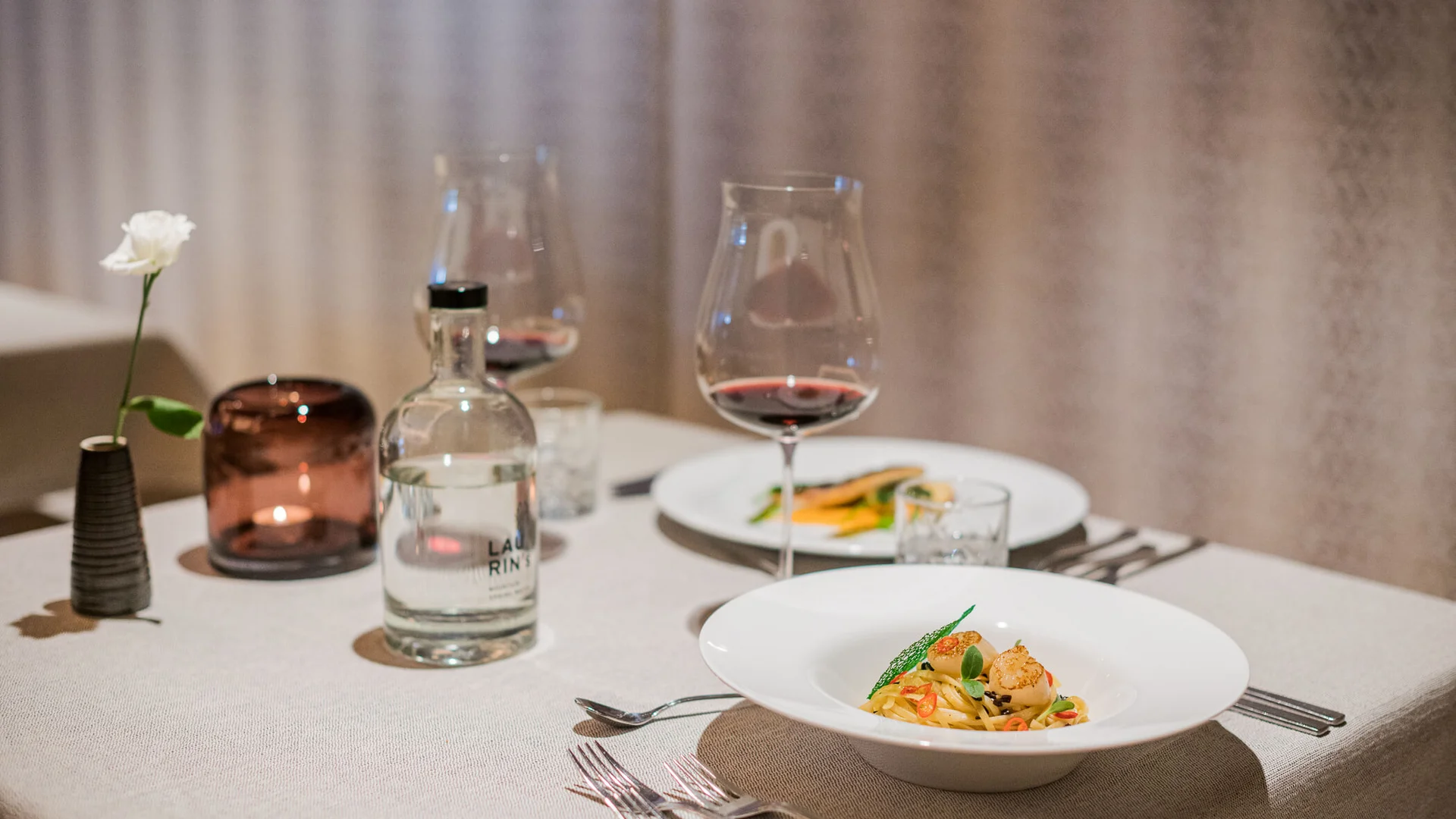 Elegantes Abendessen mit Wein, Wasserflasche und dekorativer Blume auf Tisch
