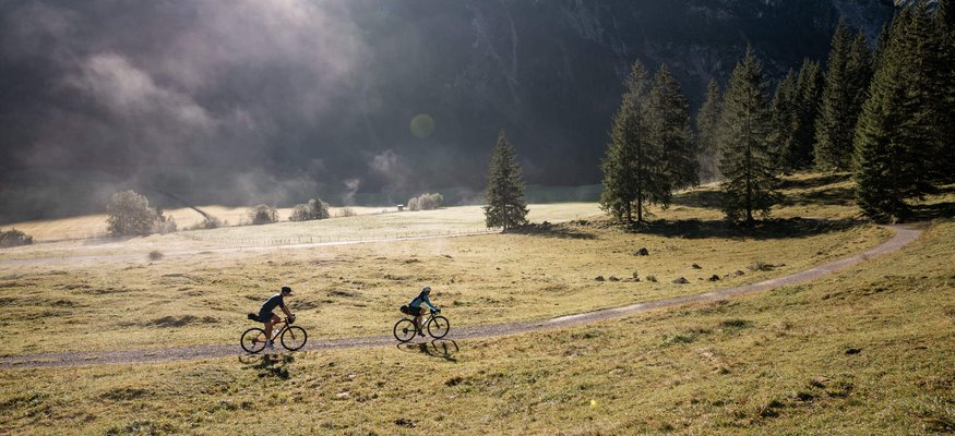Zwei Radfahrer fahren auf einem Weg durch eine bergige Wiese bei Sonnenlicht
