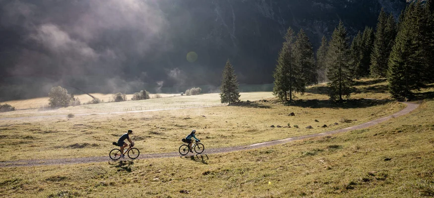 Gravelbike-Wochenende des Jahres:
Ride’n Gravel Testival 2026 © Andreas Vigl Zwei Radfahrer fahren auf einem Weg durch eine bergige Wiese bei Sonnenlicht