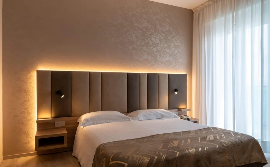 Modernes Hotelzimmer mit großem Bett und indirekter Beleuchtung am Kopfteil