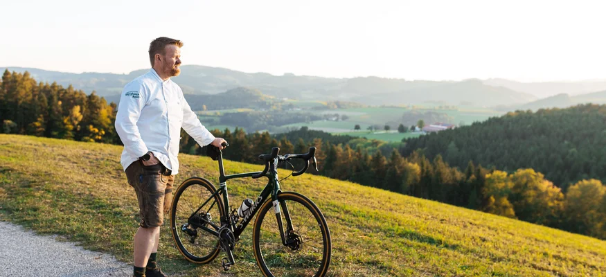 Gravel week Bucklige Welt © Niederösterreich Werbung - Mara Hohla Man with road bike standing on path overlooking hills and forest
