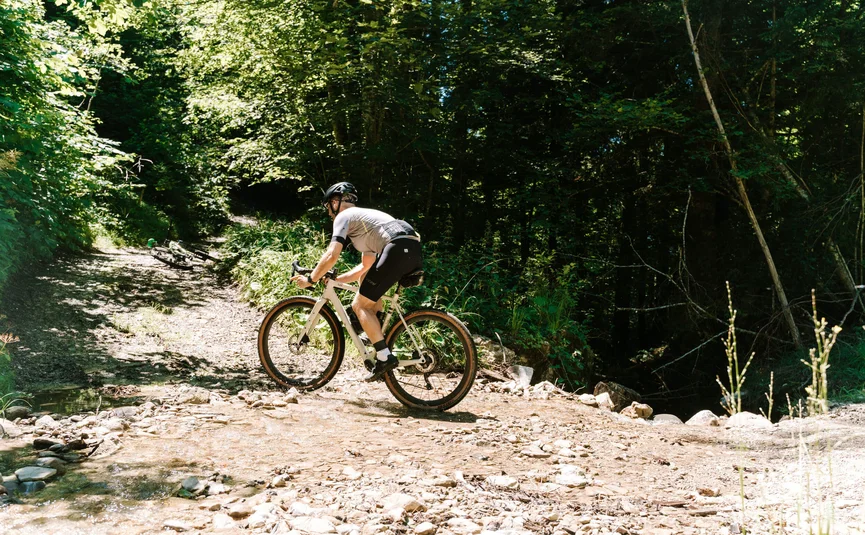 Fahrradfahrer fährt durch einen flachen Bach in einem Wald