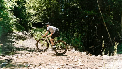 Fahrradfahrer fährt durch einen flachen Bach in einem Wald